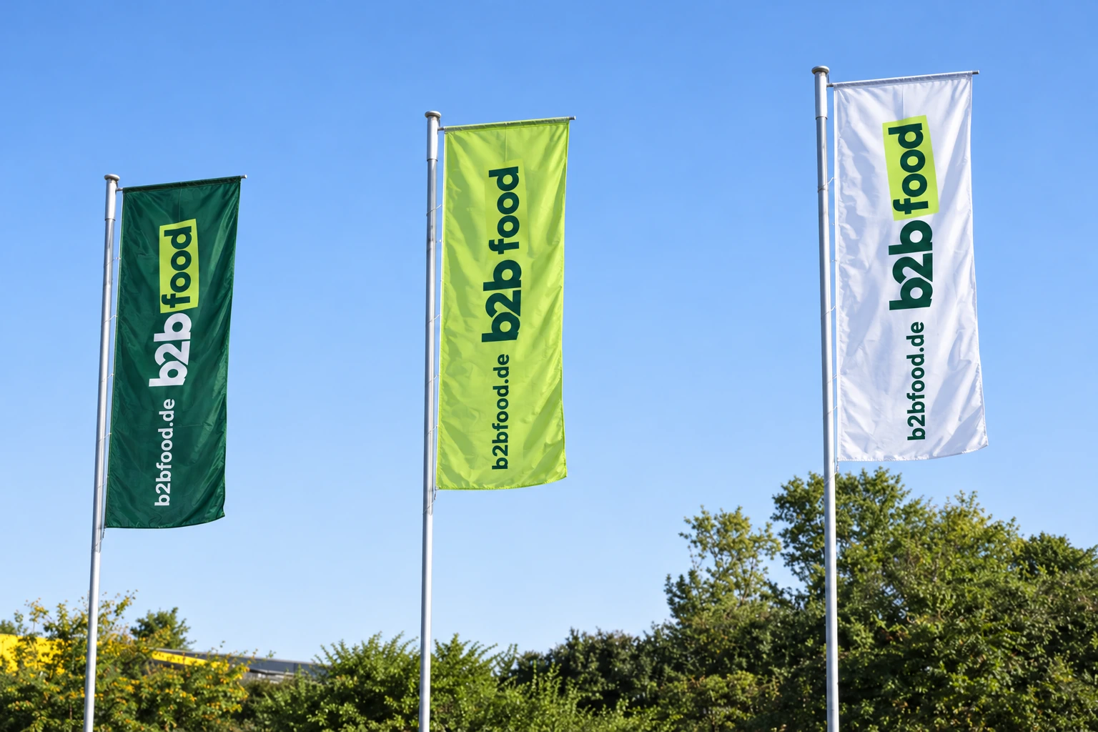 Drei b2bfood.de-Fahnen in Dunkelgrün, Hellgrün und Weiß vor blauem Himmel
